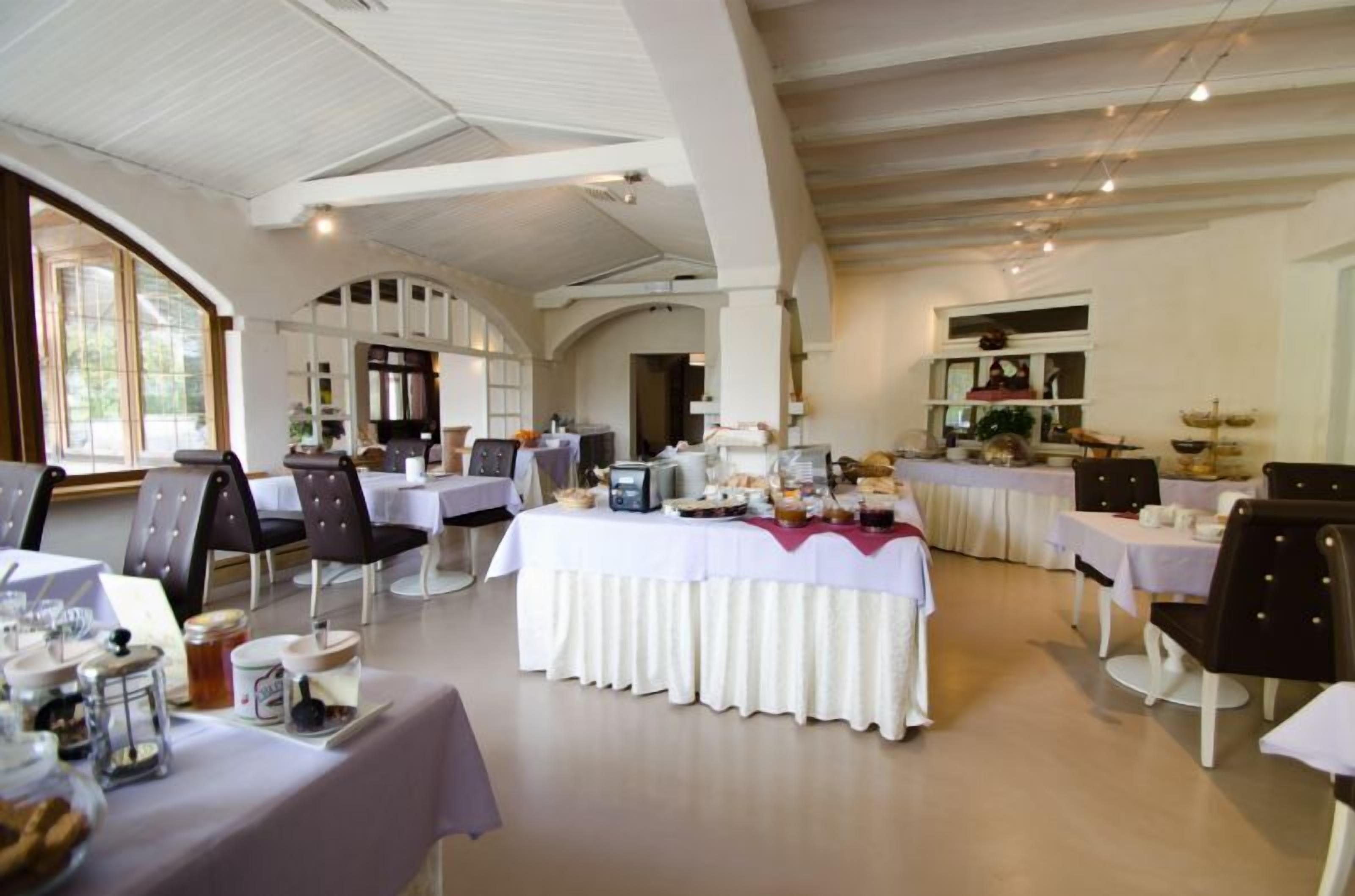 A spacious dining area with high ceilings and arched windows, featuring multiple tables set for dining.