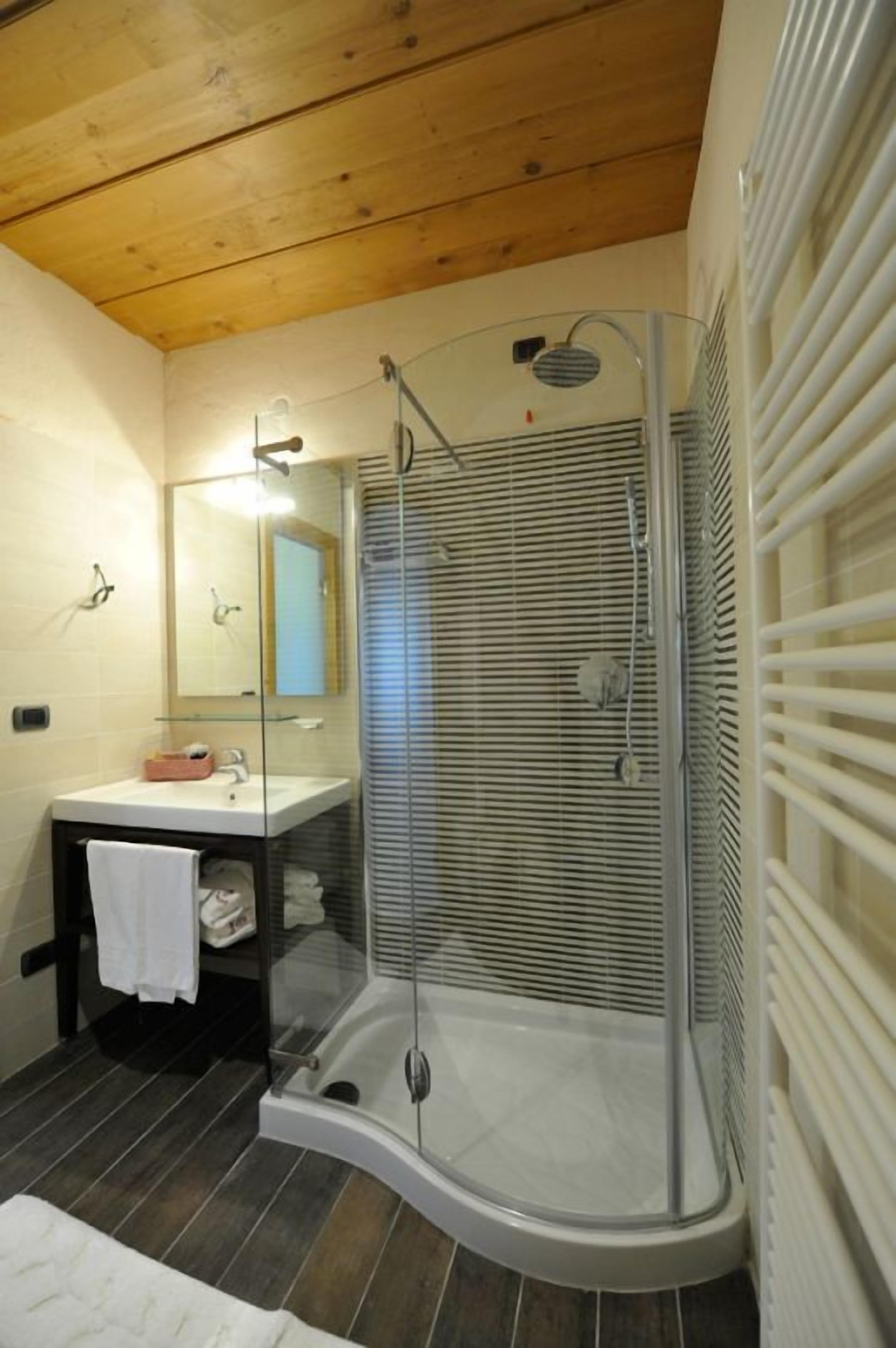 Un baño moderno con ducha de vidrio, lavamanos blanco y techo de madera.
