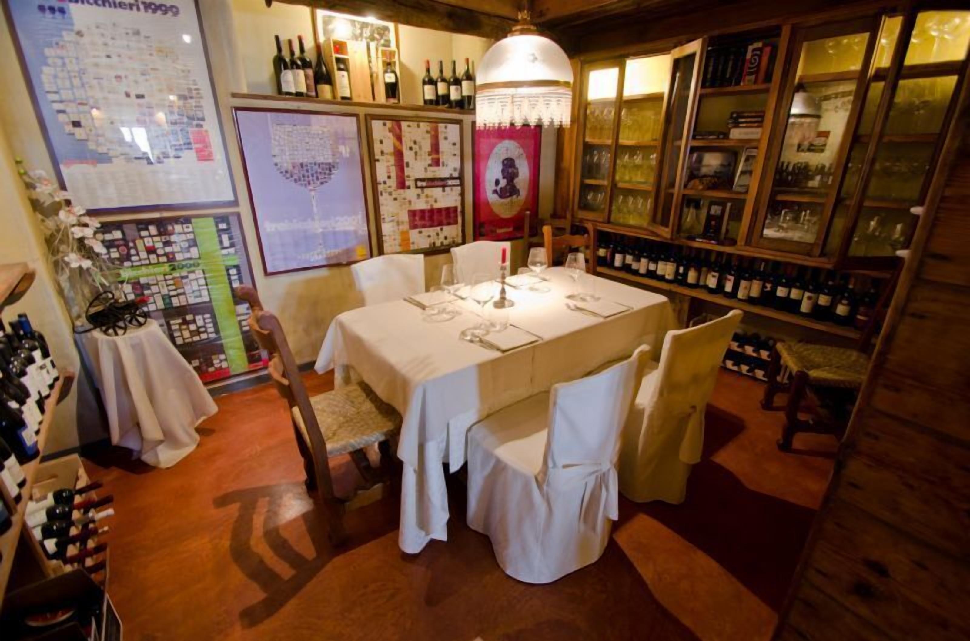 Un coin repas avec une table dressée pour quatre personnes, entourée de chaises. On aperçoit des bouteilles de vin sur des étagères et un porte-bouteilles à l’arrière-plan.
