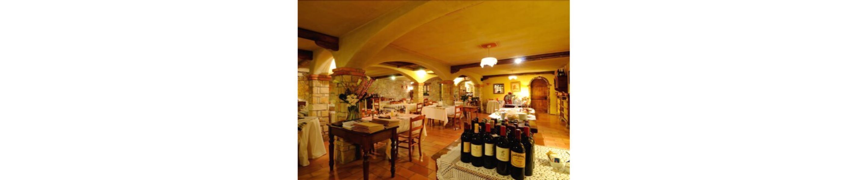 A restaurant with tables and chairs, a counter with wine bottles, and a stone wall.