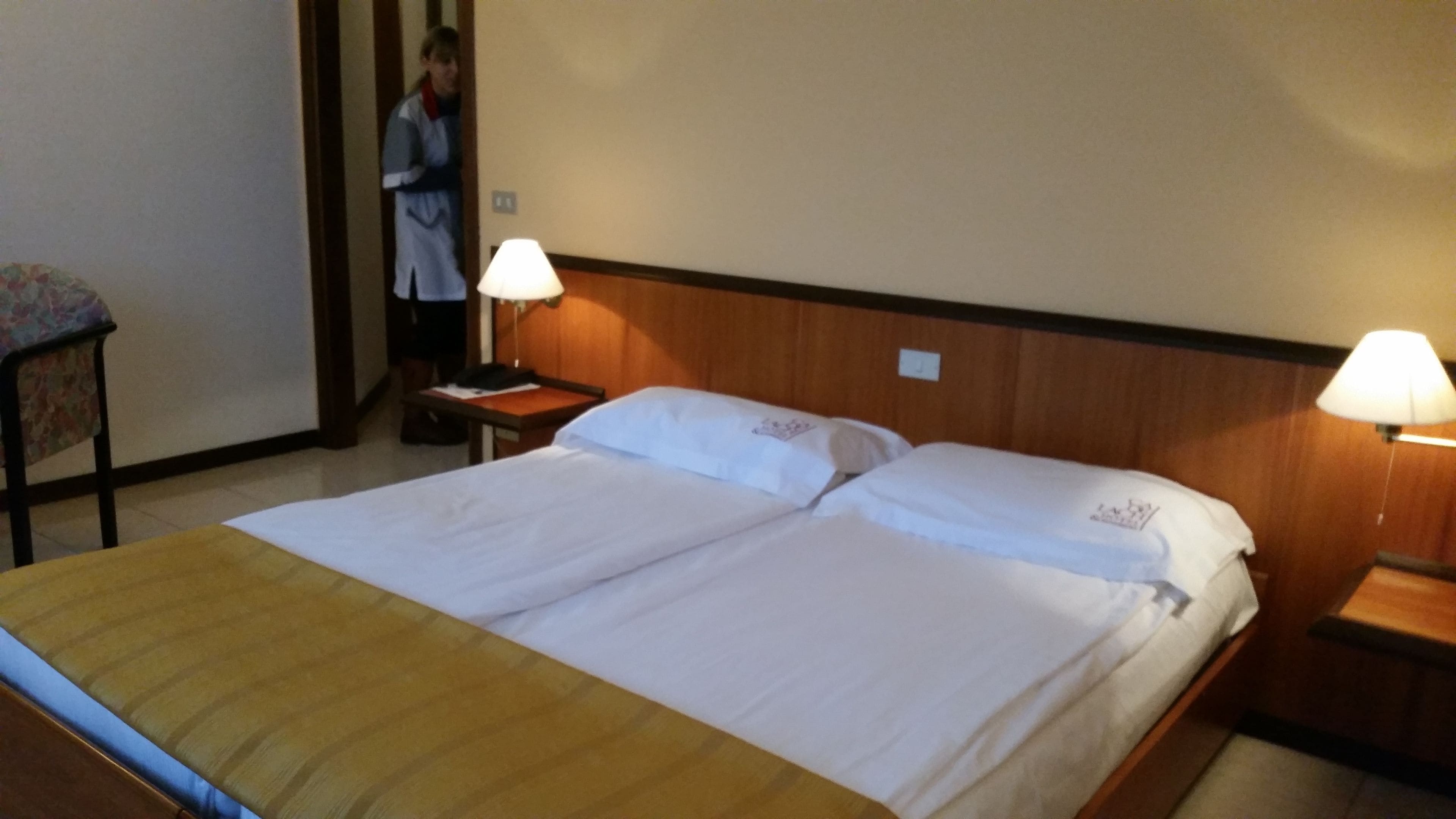 A hotel room with two beds, each with a pillow and a nightstand with a lamp.