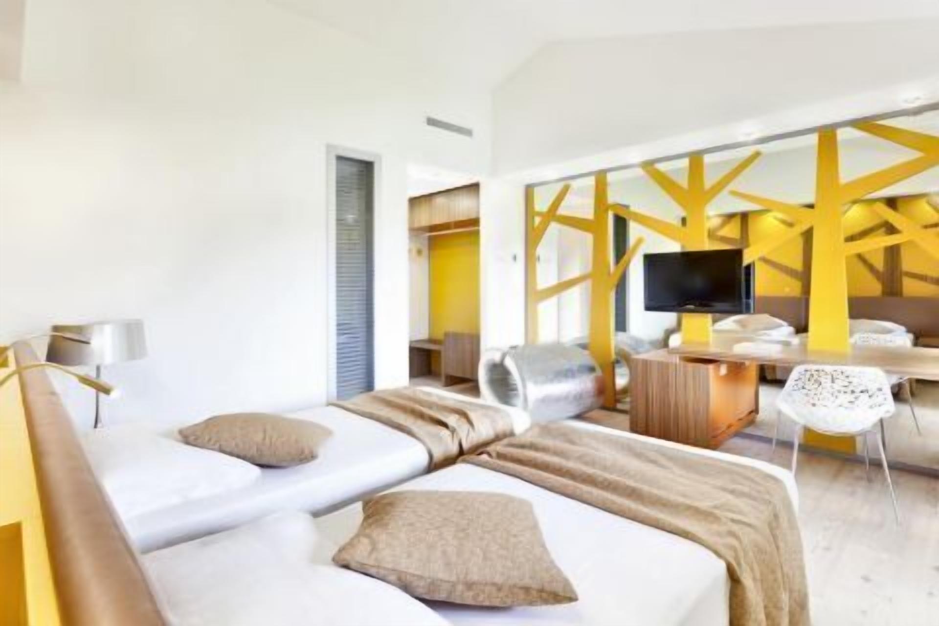 Quarto de hotel com duas camas, uma televisão, uma escrivaninha e uma cadeira.
