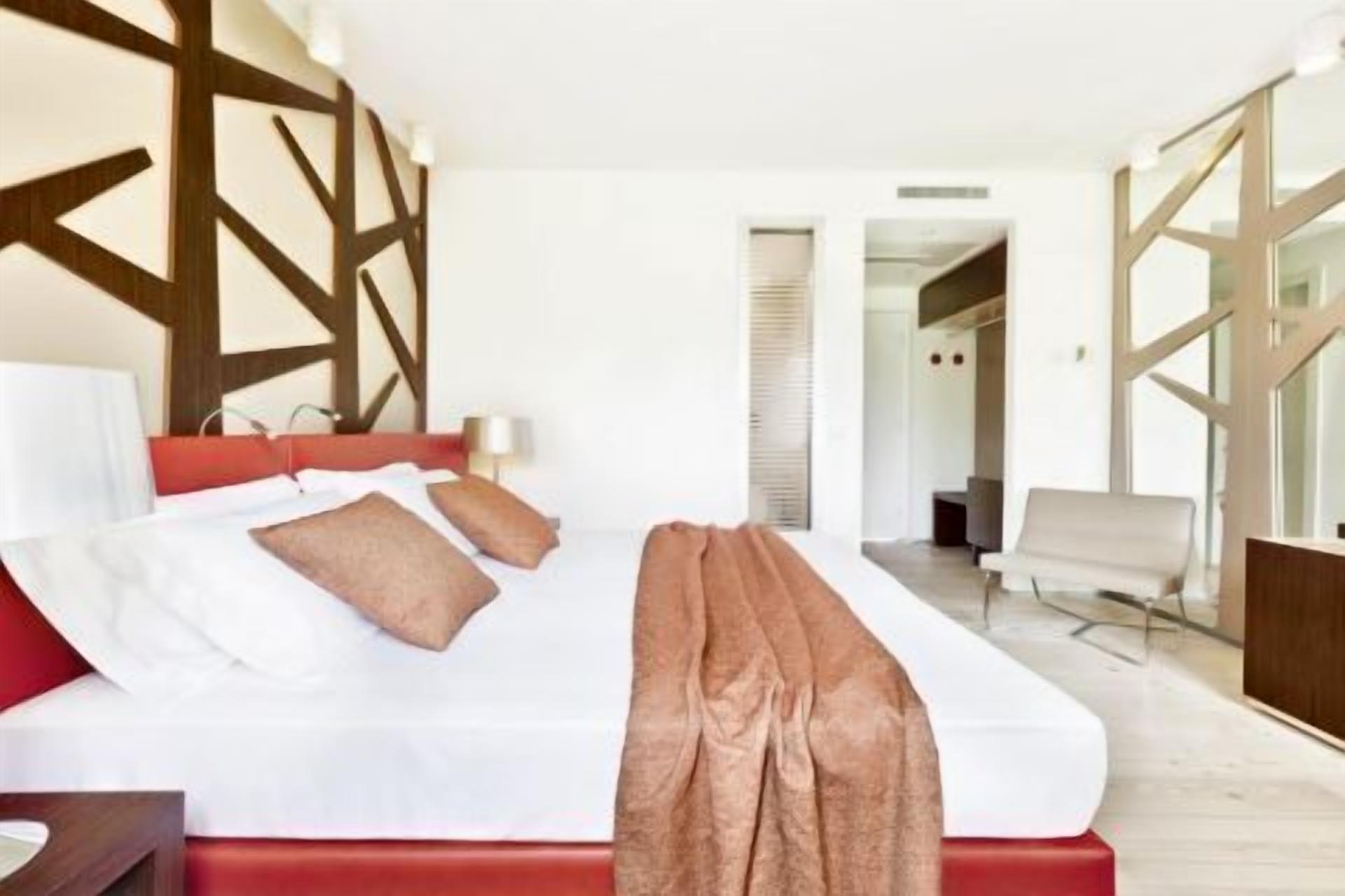 A modern hotel room with a large bed, a red headboard, and a wooden wall design.