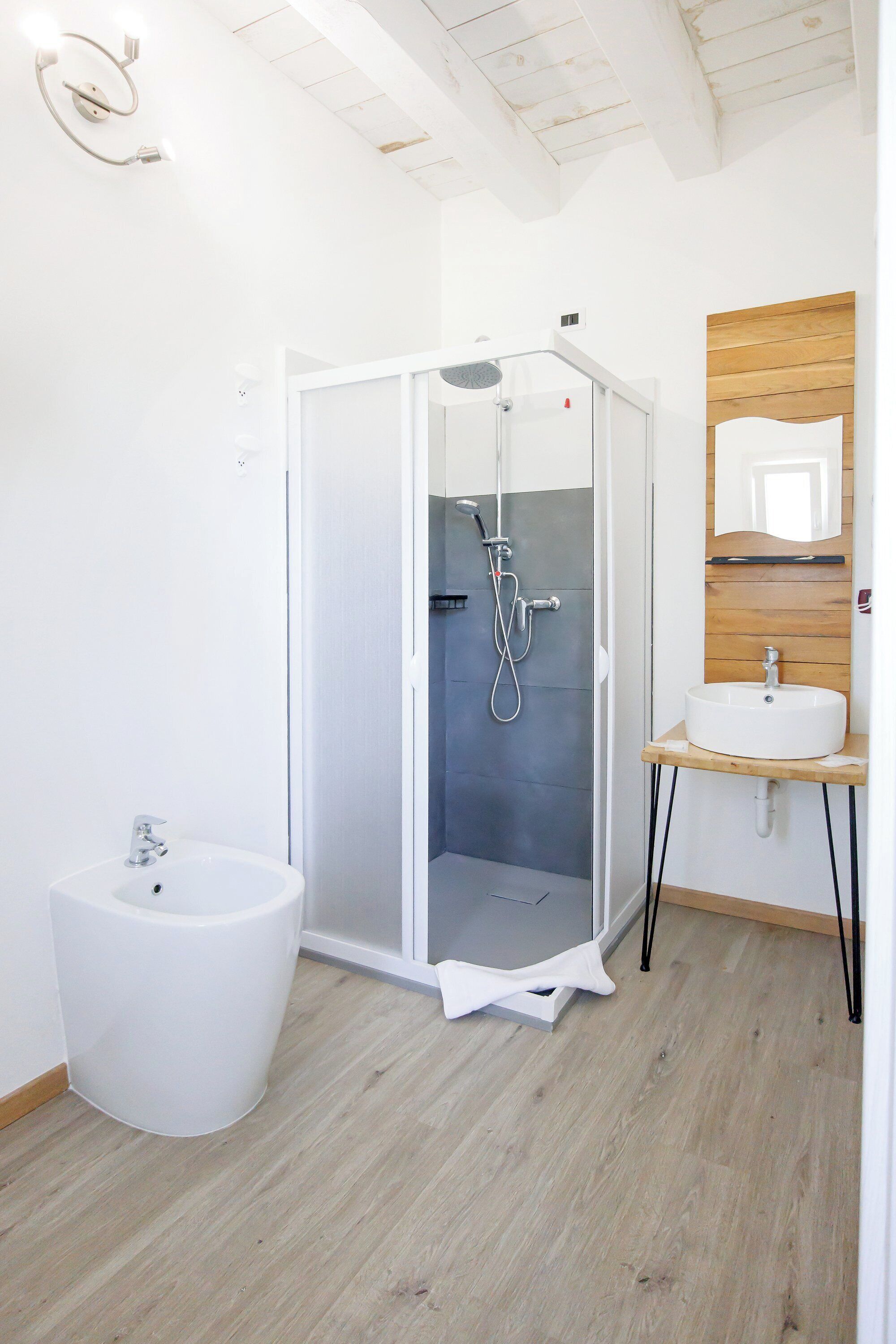 Ein modernes Badezimmer mit einer gläsernen Duschkabine, einem weißen Waschbecken und einem Holz-Waschtisch.