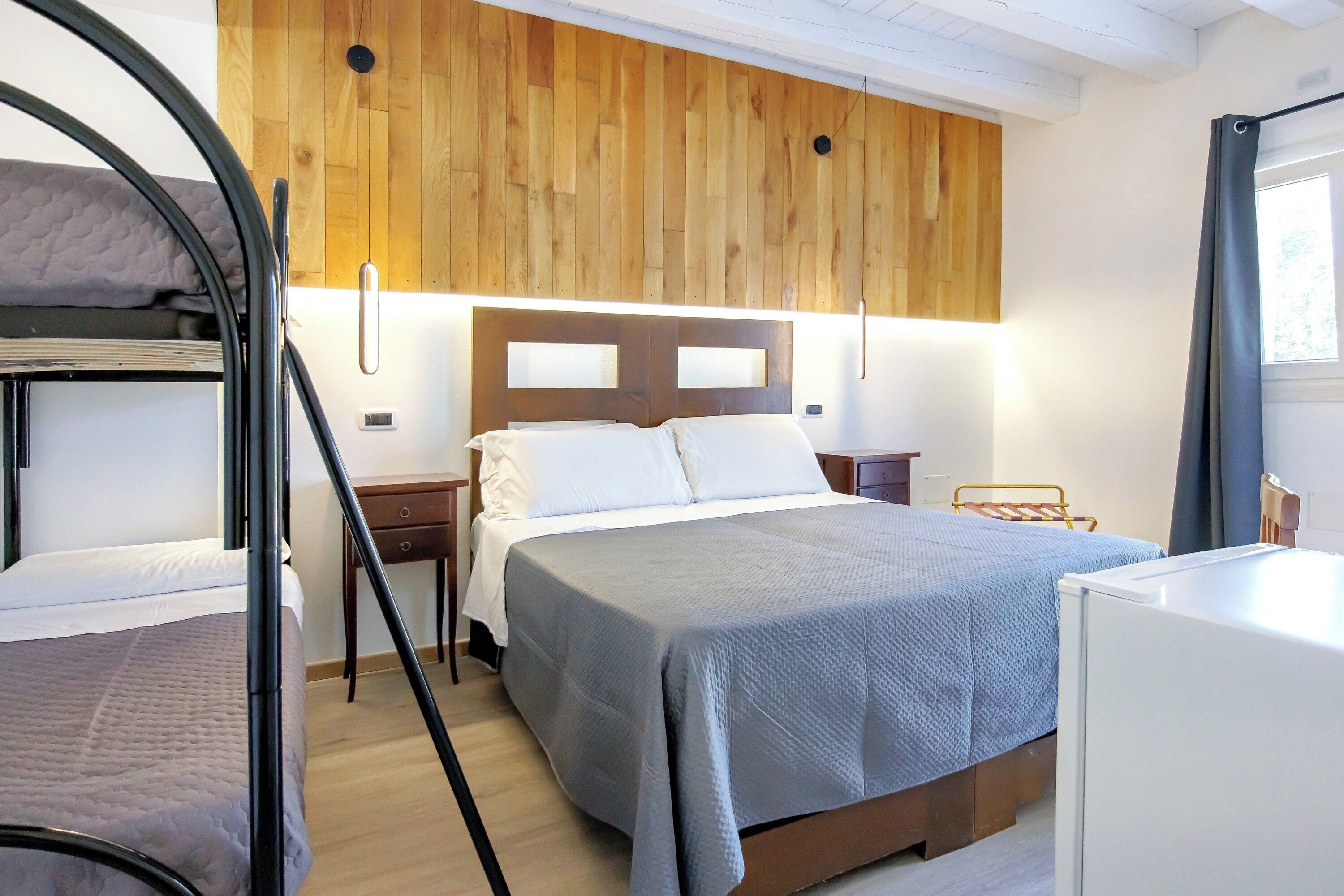 Un dormitorio con literas, una cama individual, paneles de madera en la pared, una mesita de noche y un escritorio pequeño.