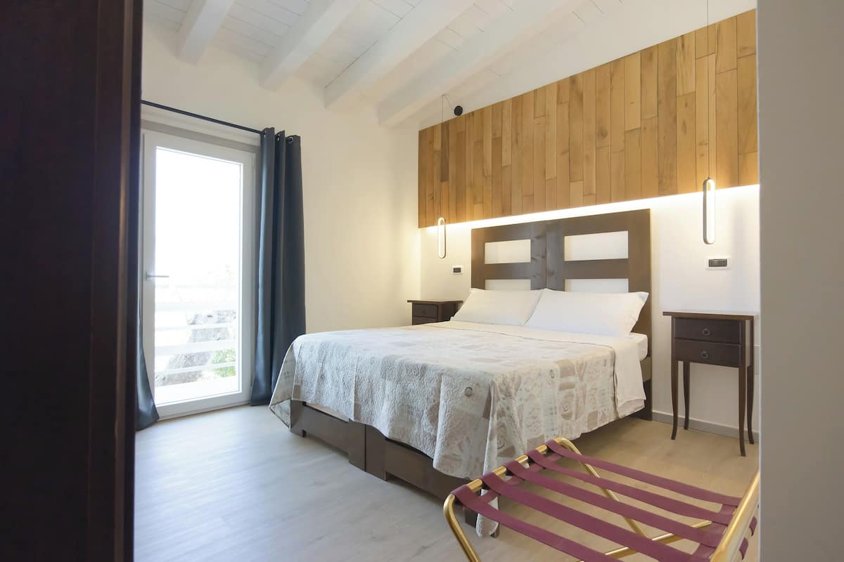 A bedroom with a bed, a wooden headboard, a bedside table, and a window with curtains.