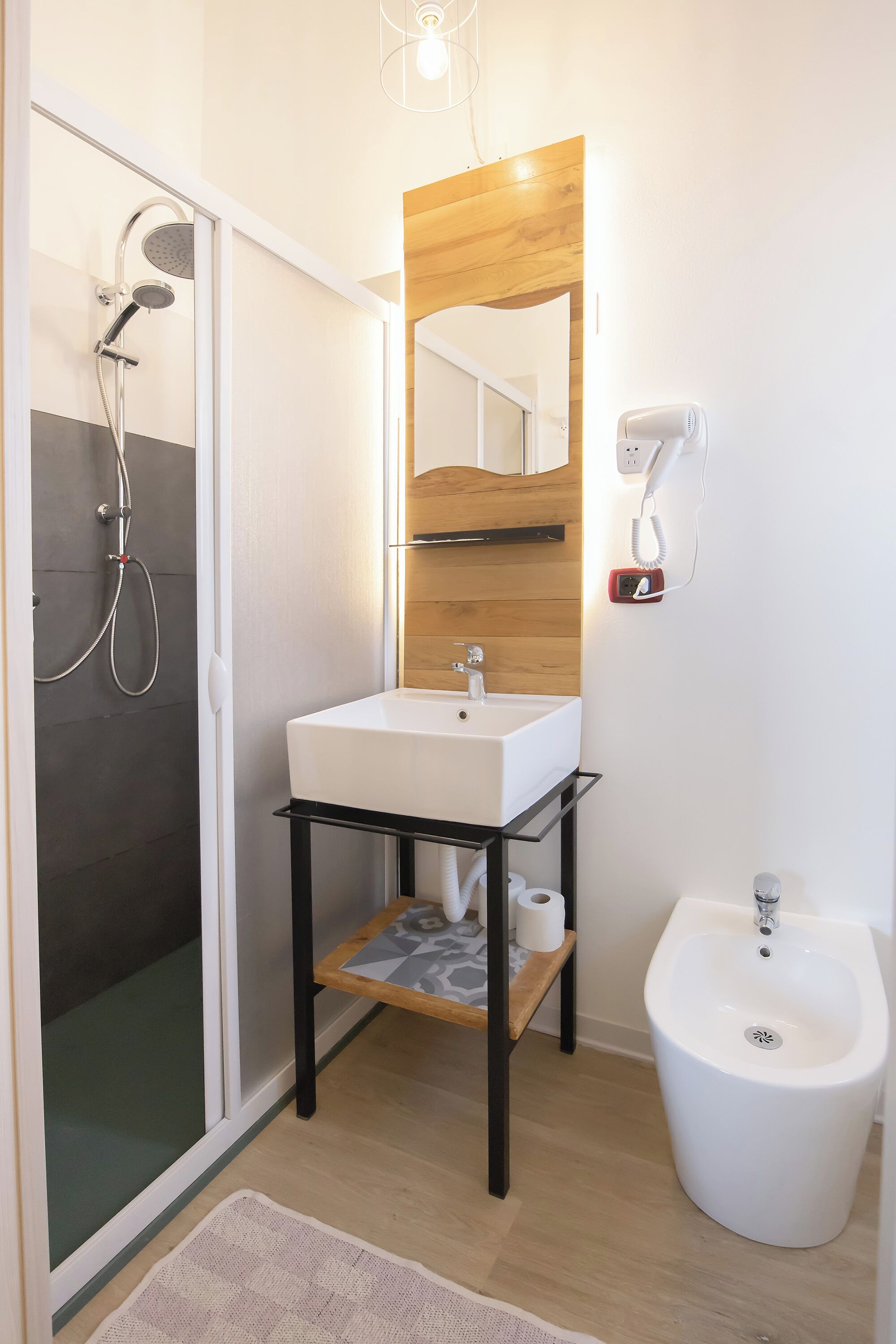 A modern bathroom with a glass-enclosed shower, a white sink with a wooden countertop, a bidet, and a mirror with a wooden frame.