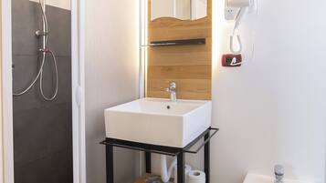 A modern bathroom with a glass-enclosed shower, a white sink with a wooden countertop, a bidet, and a mirror with a wooden frame.