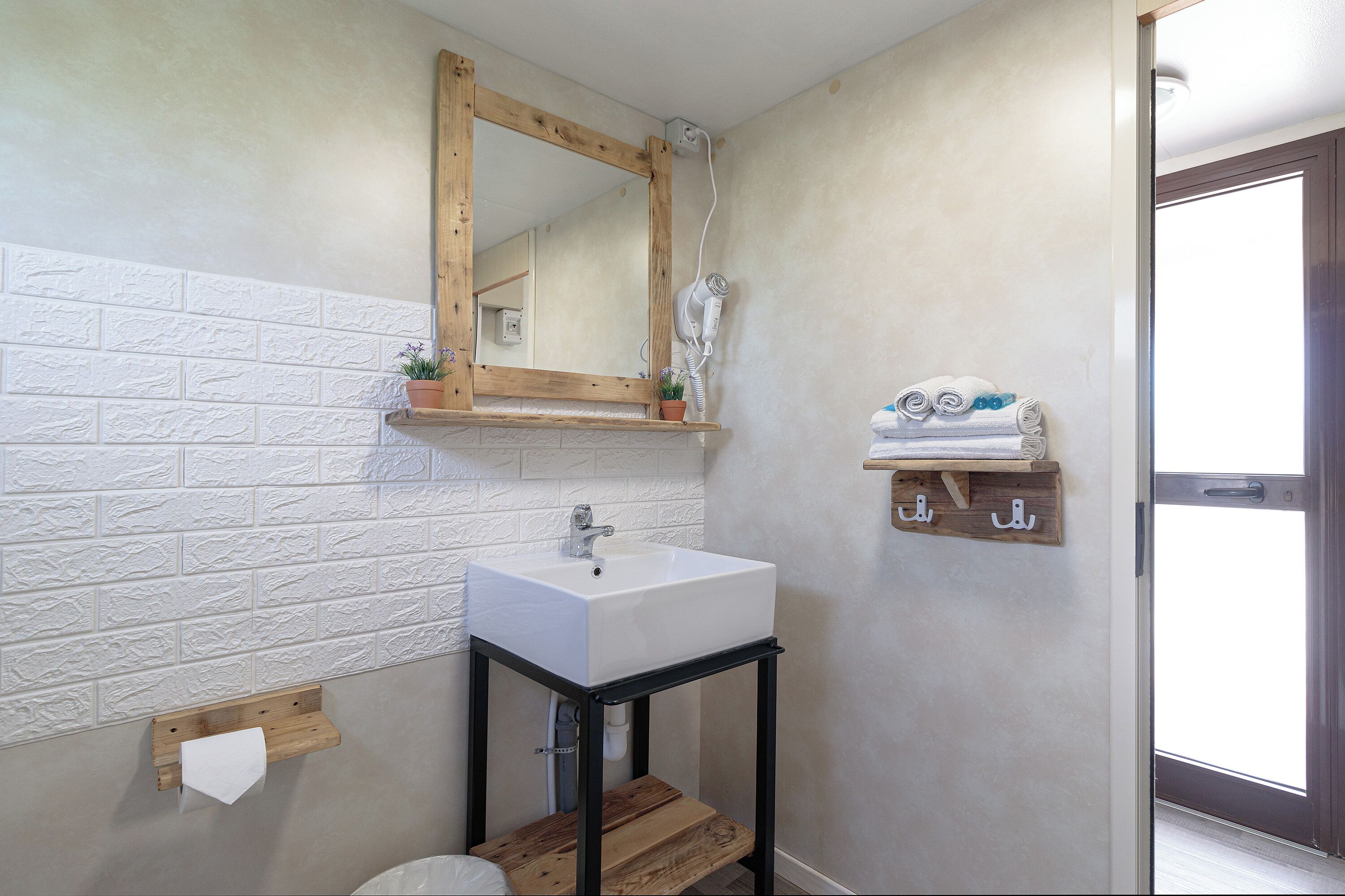 Un baño con un lavamanos blanco, estante de madera y un espejo.