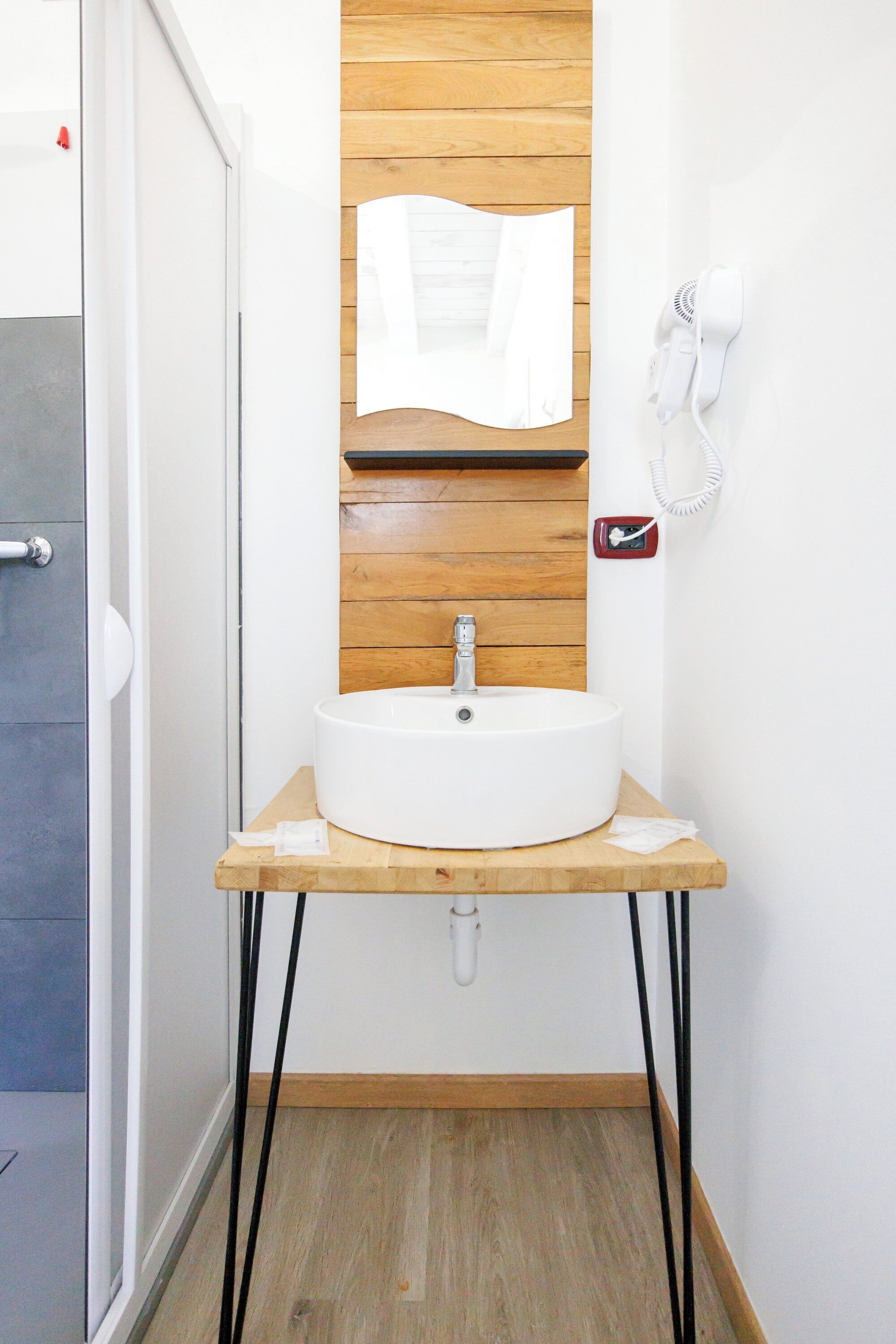 Een badkamer met een witte wastafel op een houten plank, een handdoek aan de muur en een haardroger.