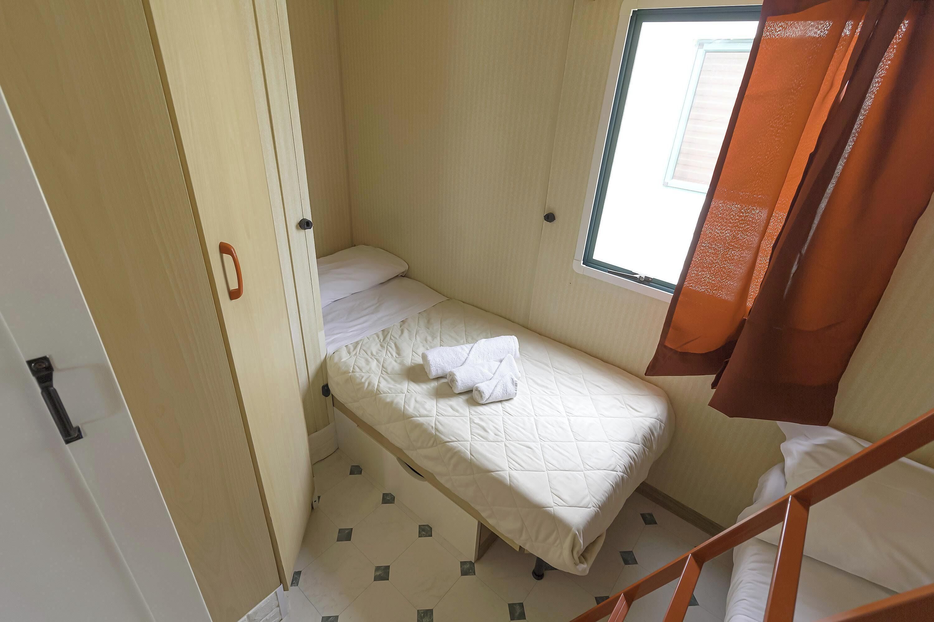 Quarto pequeno com uma cama de solteiro, janela e porta.
