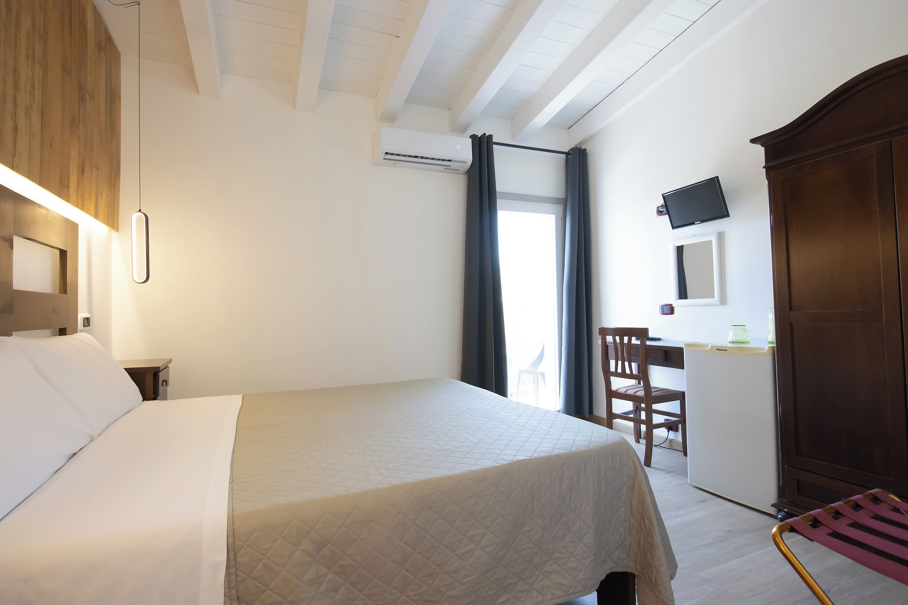 A hotel room with a bed, a desk, a chair, a television, and an air conditioning unit.
