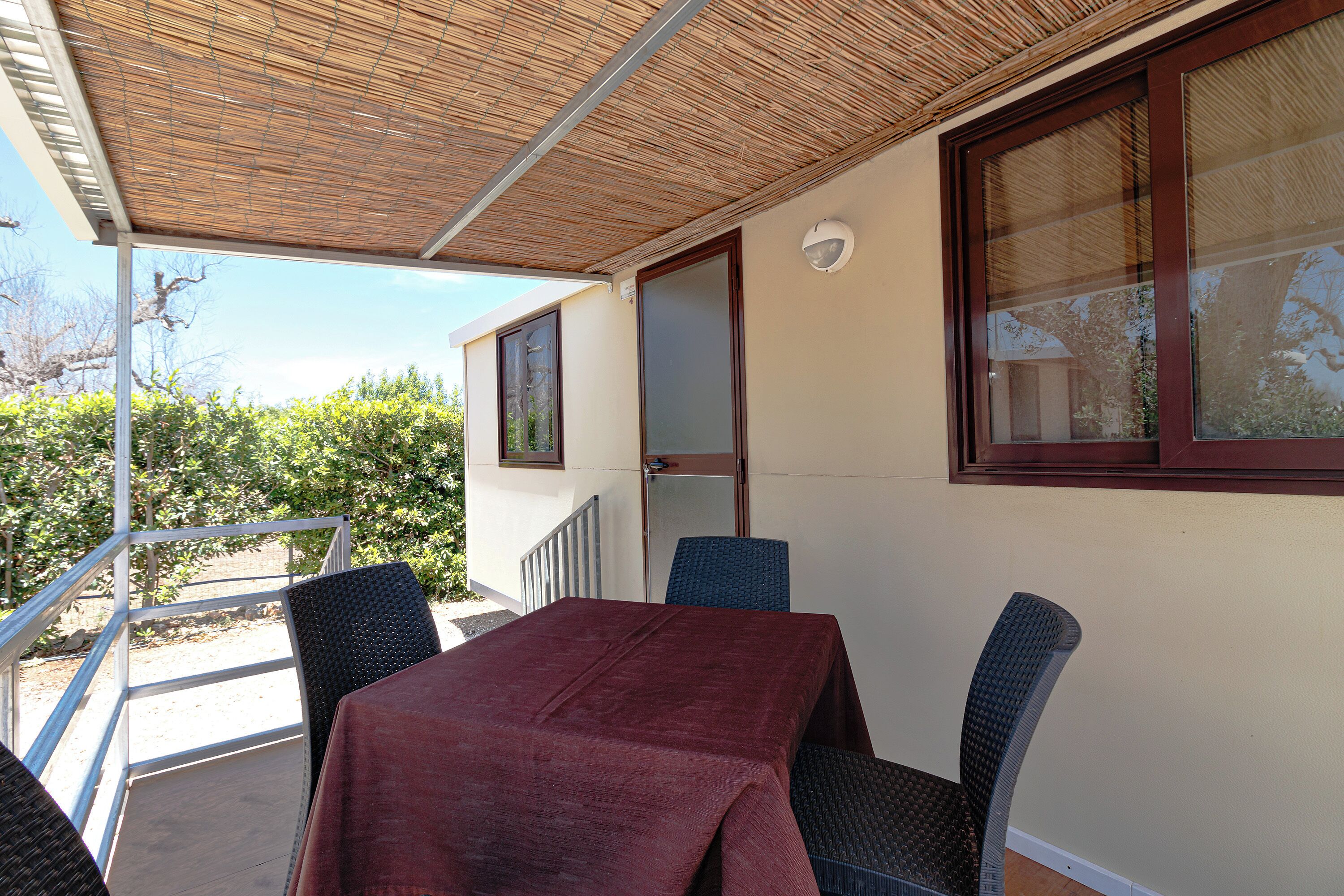 A covered outdoor seating area with a table and chairs, a door, and a window.