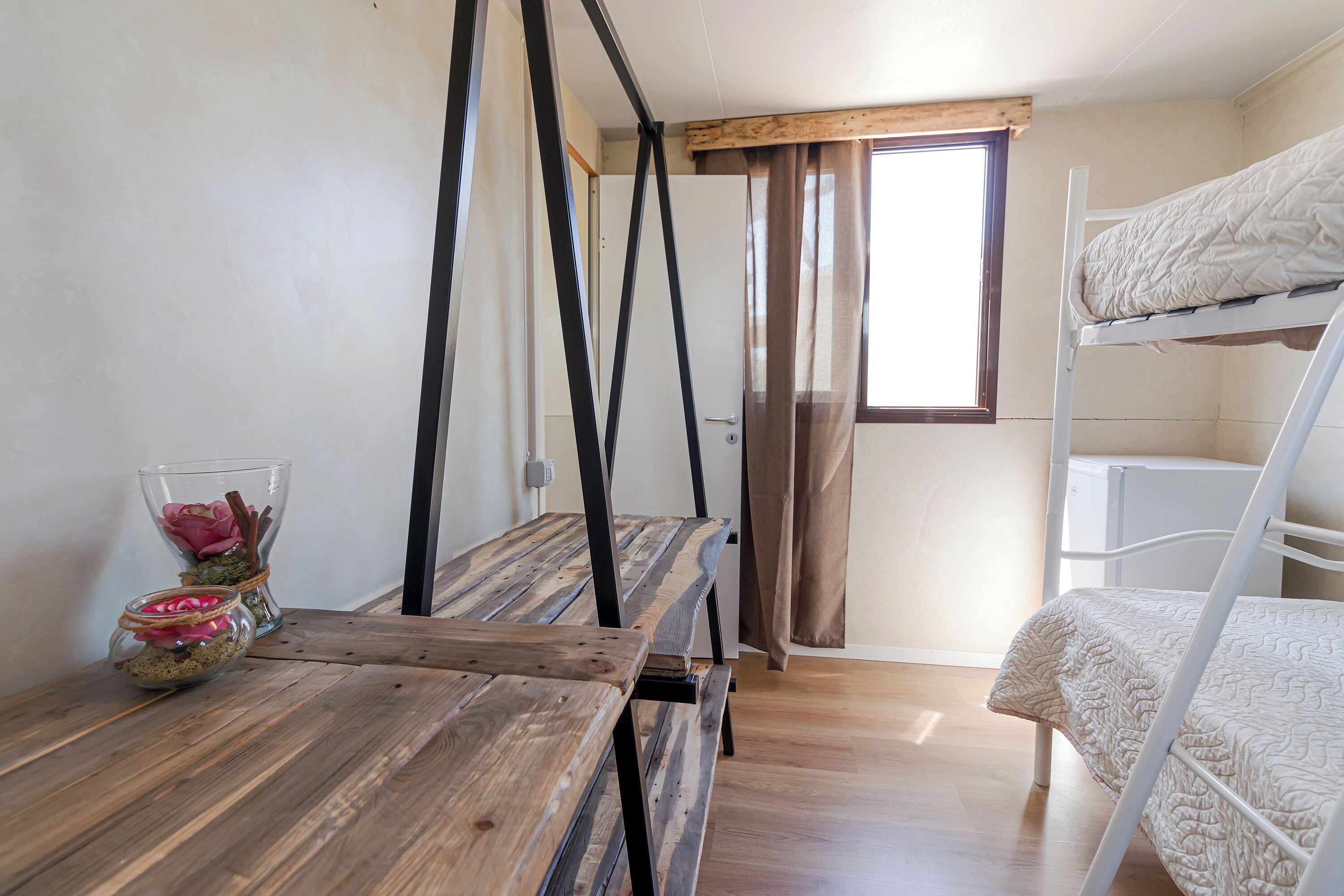 A bunk bed room with a wooden table and a glass vase with flowers.
