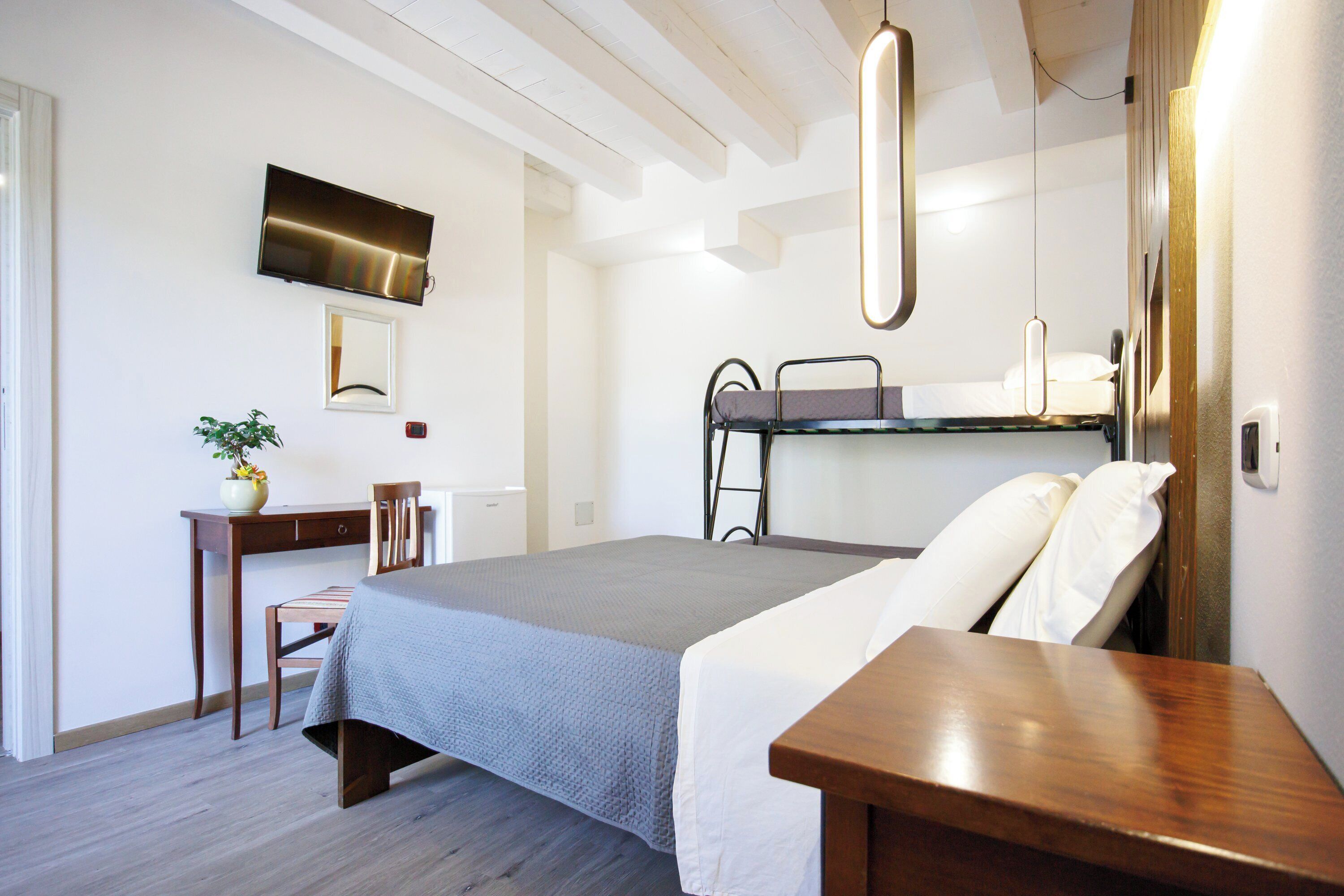 A bedroom with a bed, bedside table, desk, chair, TV, and a small plant.