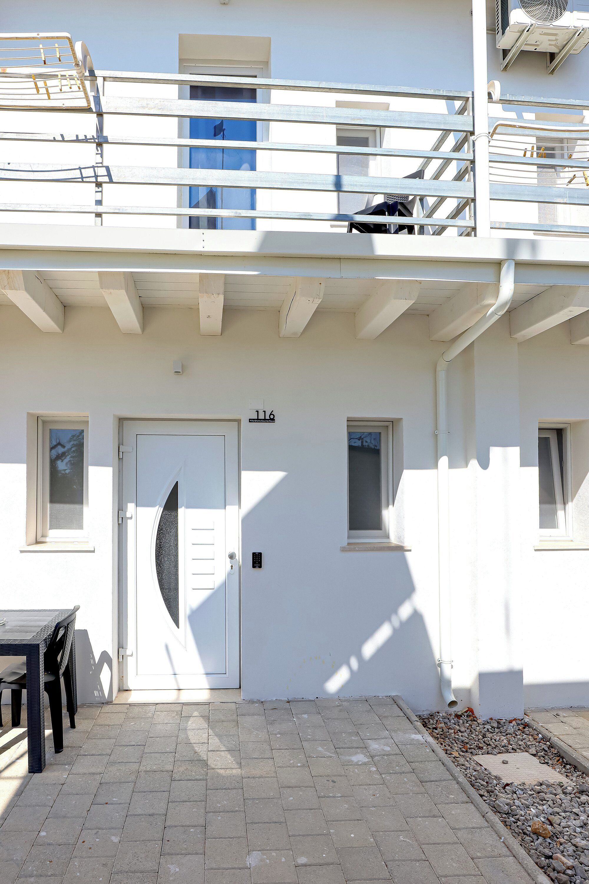 A white building with a door marked "116", a small window, and a balcony with a railing.