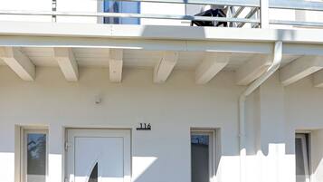 A white building with a door marked "116", a small window, and a balcony with a railing.