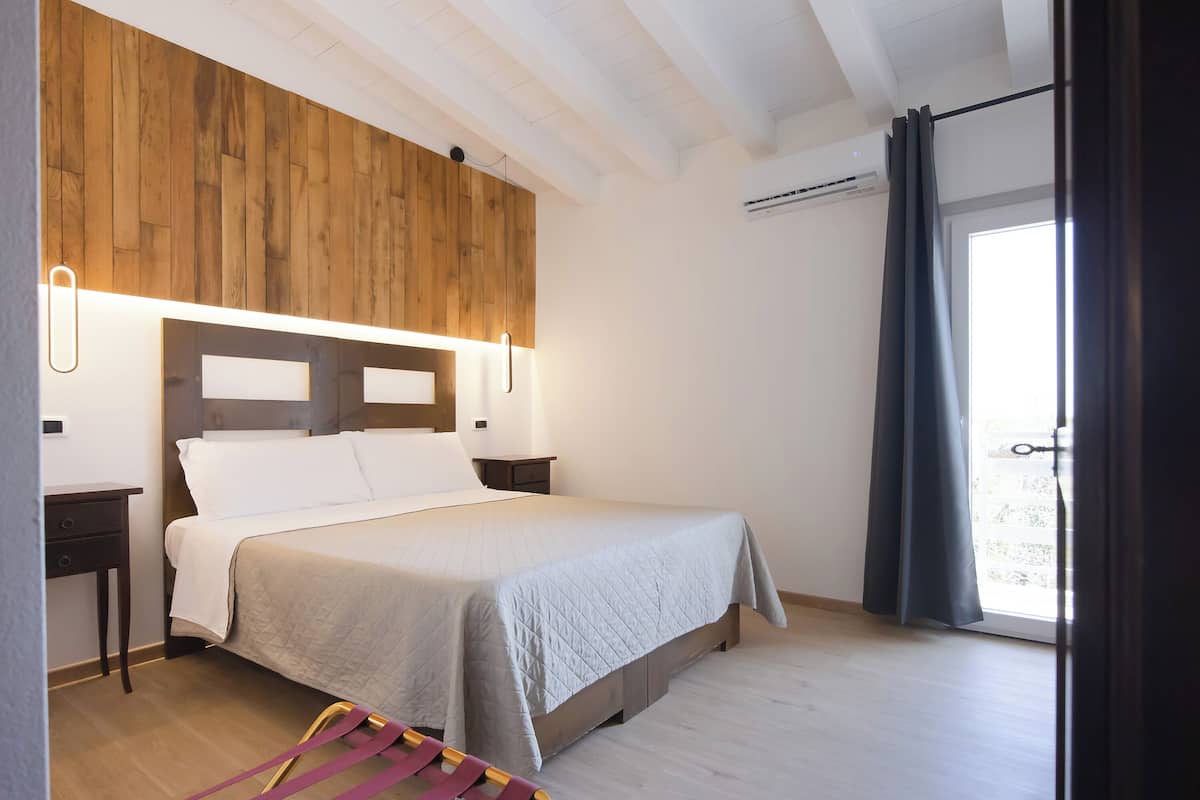 A bedroom with a wooden headboard, a bed with white bedding, a nightstand, and a window with curtains.