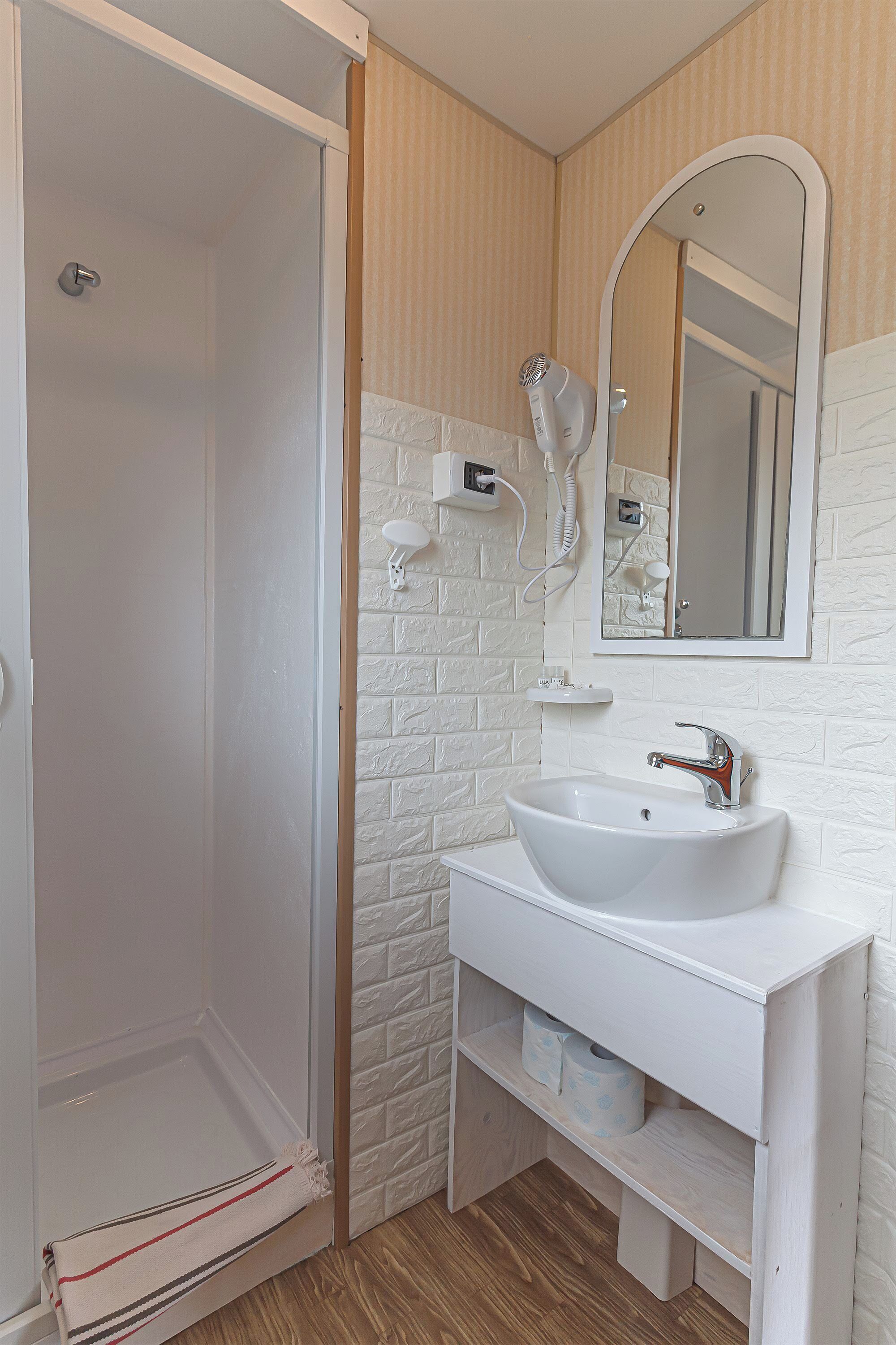 Un bagno con un lavandino bianco, uno specchio e una doccia.