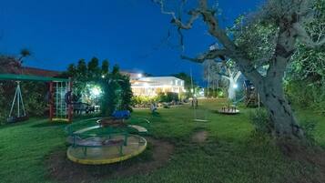 A well-lit outdoor area with a swing set, a round table, and a tree.