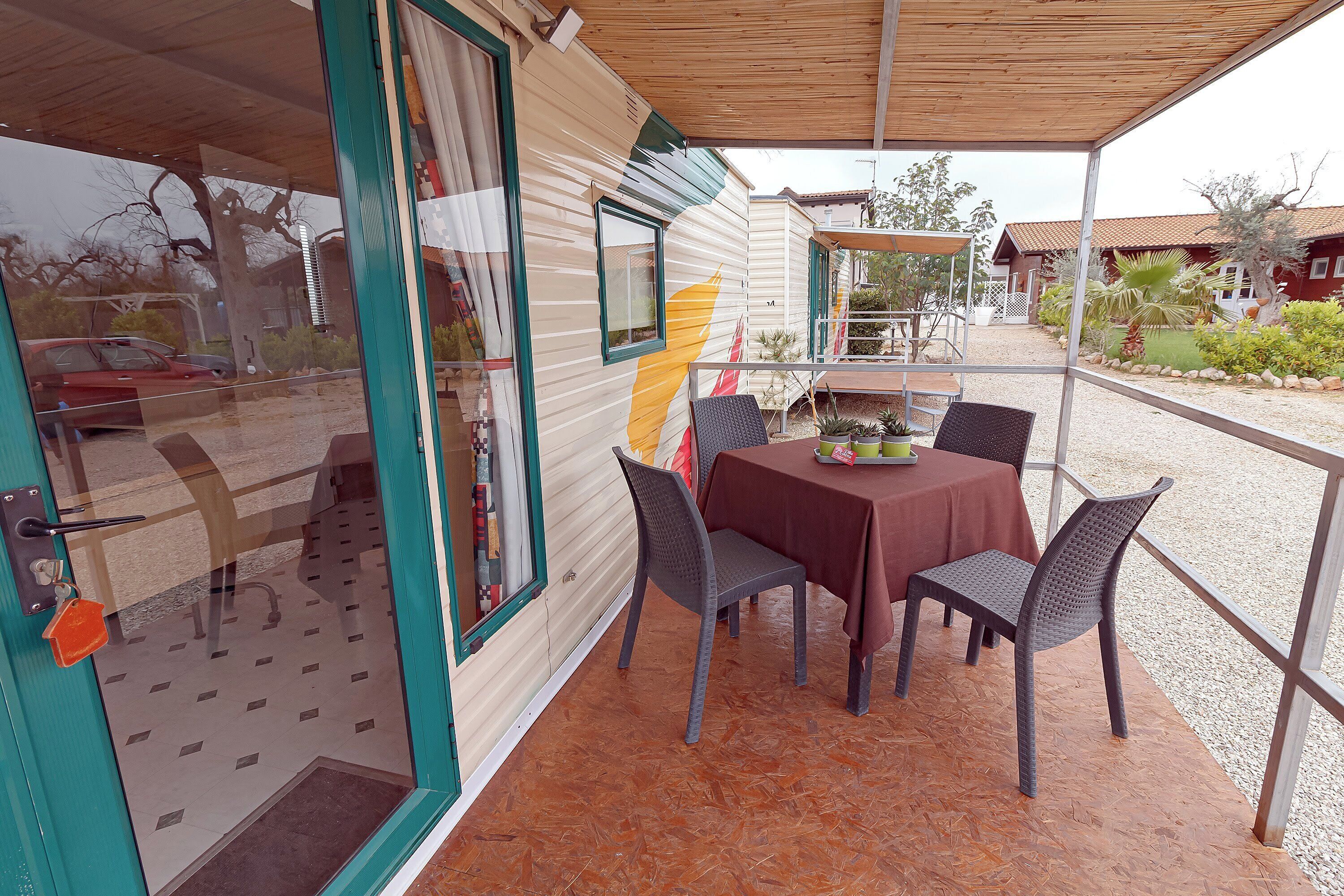 A covered patio area with a table and chairs, a door with a window, and a view of the surrounding area.