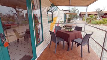 A covered patio area with a table and chairs, a door with a window, and a view of the surrounding area.