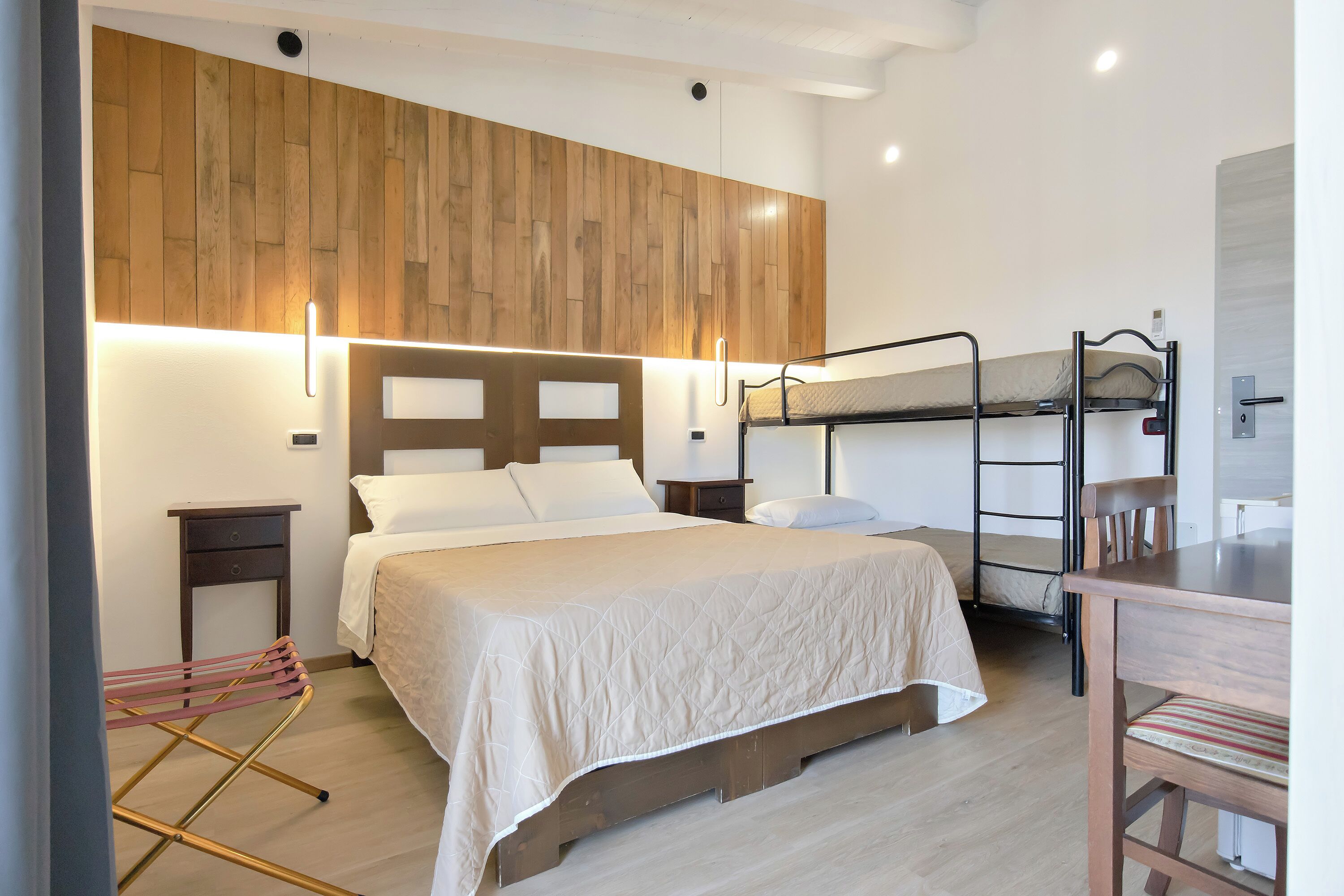 A bedroom with a bunk bed, a single bed, a wooden headboard, bedside tables, a desk, and a chair.
