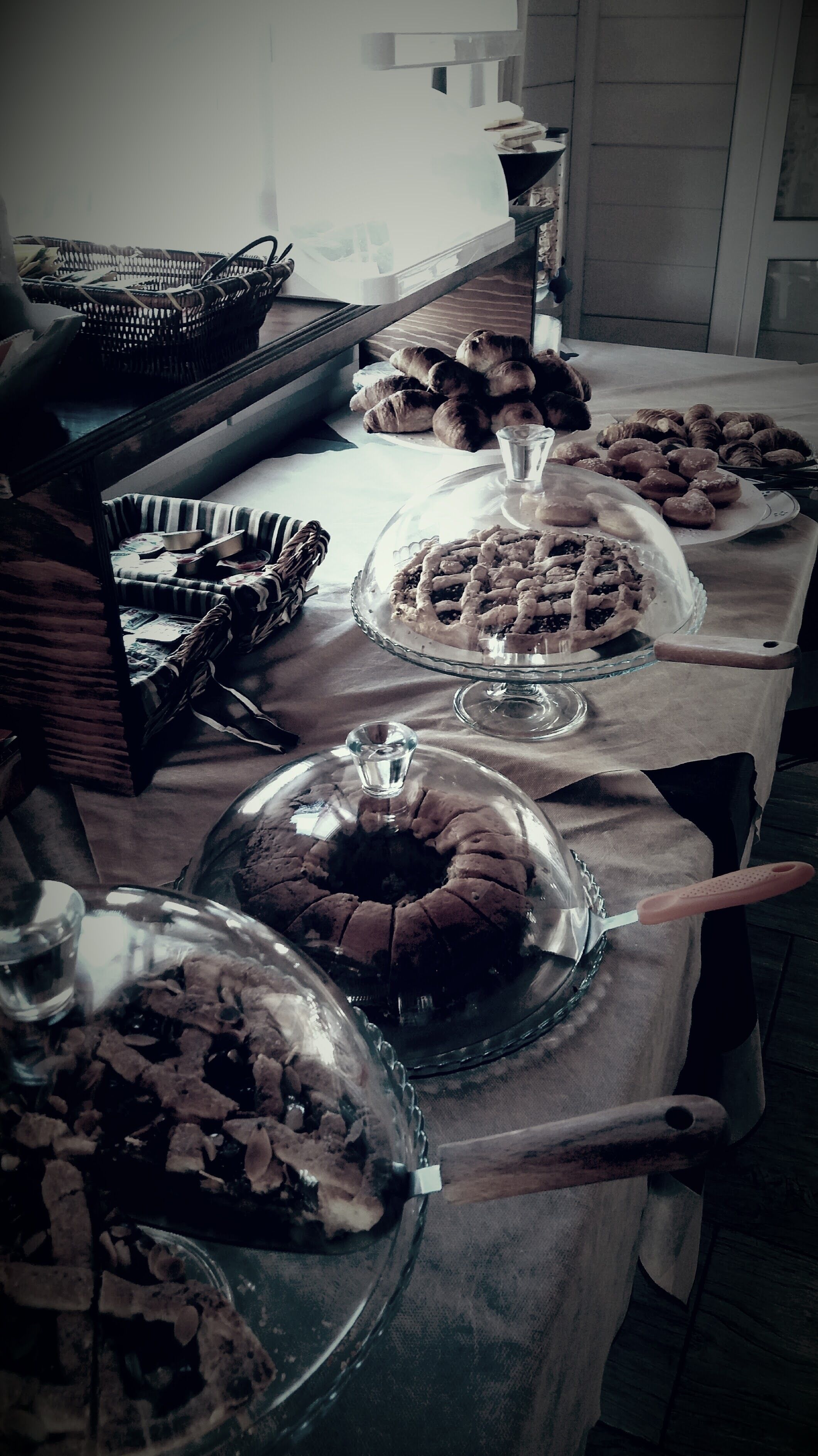 Uma mesa de buffet com diversos alimentos, incluindo tortas e doces, cobertos por cúpulas de vidro e bandejas.