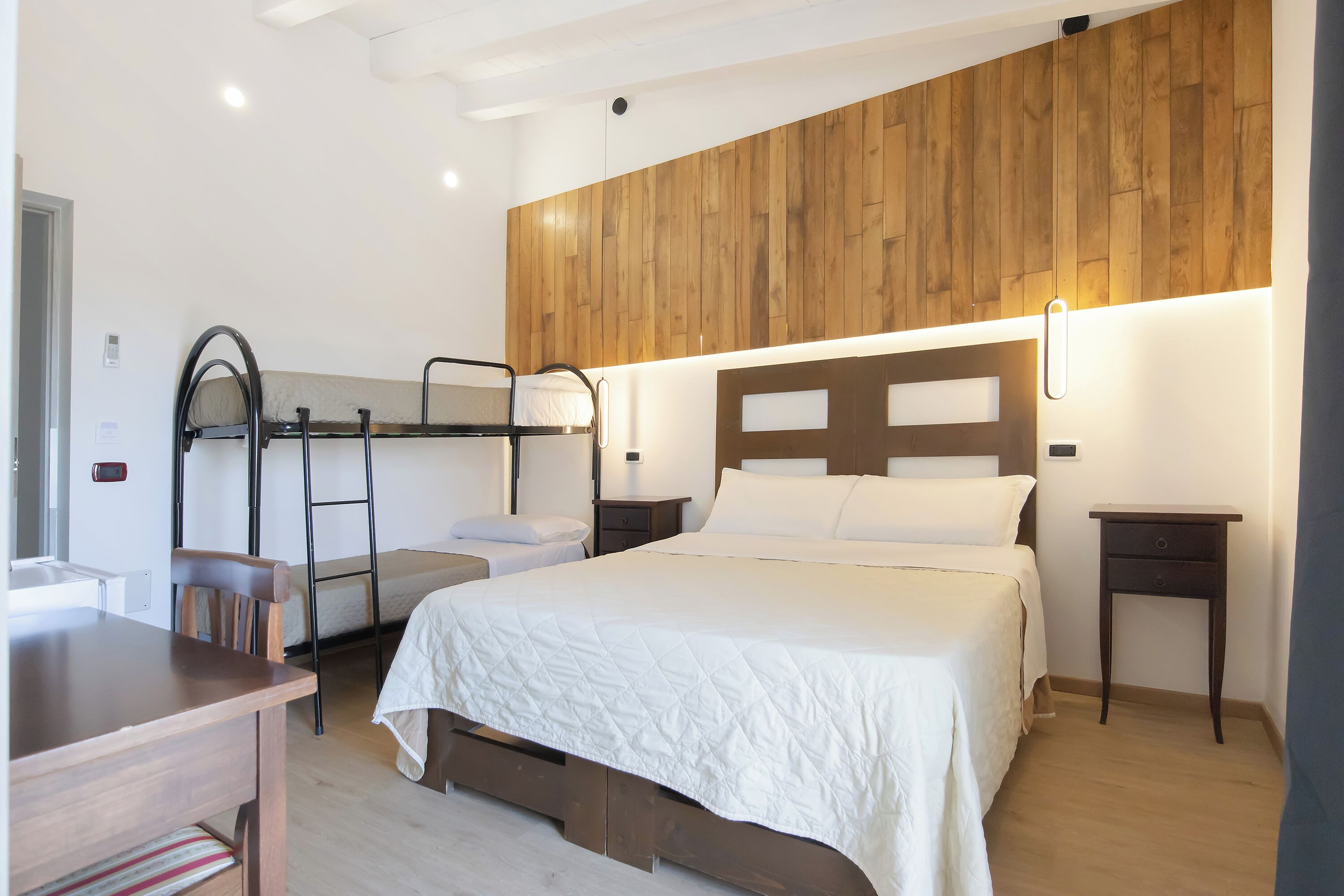 A bedroom with a bunk bed, a desk, and a wooden wall panel.