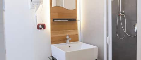 A modern bathroom with a white sink, wooden vanity, and a glass shower enclosure.