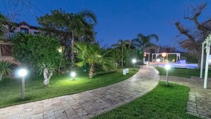 A well-lit pathway leading to a pool area with a pergola and outdoor seating. - Villa Ghetta Country House (Leverano)