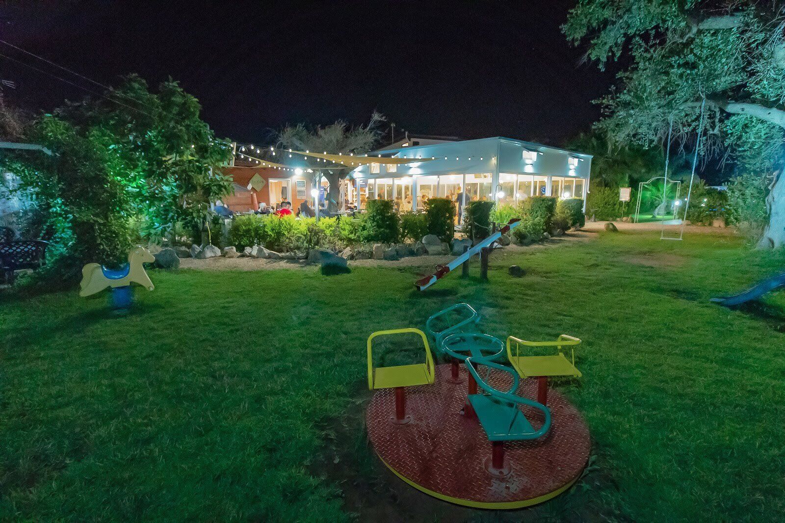 A playground with swings and a seesaw, surrounded by a well-maintained lawn and trees.