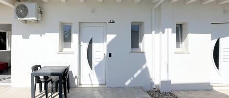 A white building with a door marked "116", a table with chairs, and an air conditioning unit mounted on the wall.