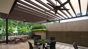 Un patio al aire libre con una mesa y sillas, ventiladores de techo y vistas a zonas verdes.