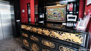 Una recepción con elaborados detalles dorados, una obra de arte enmarcada sobre ella y un muro negro y rojo.