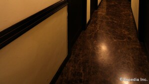 Un pasillo con puertas de madera oscura, paredes blancas y piso de mármol. Hay apliques que proporcionan luz.