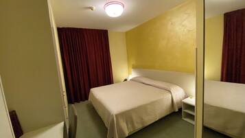 Una camera d'albergo con un letto singolo, un comodino e uno specchio.