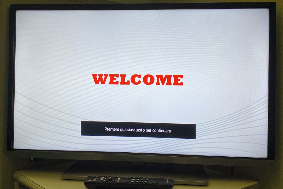 Ein Fernsehbildschirm mit der Aufschrift 'WELCOME' und der Aufforderung 'Premere qualsiasi tast per continuare' in einem Hotel-Empfangsbereich.