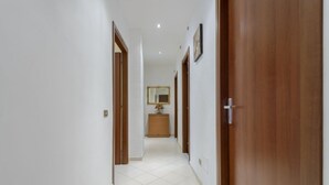 Un pasillo con piso de baldosas blancas, puertas de madera y un pequeño armario de madera a lo lejos.