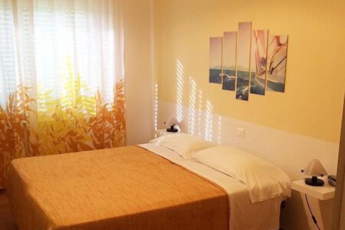 A hotel room with a large bed, a bedside table, a lamp, and a wall with three framed pictures.