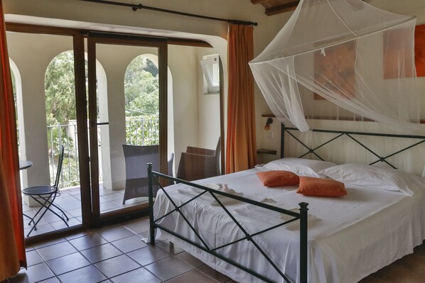 A room with a bed, a balcony with a chair, and a view of greenery. - Hotel Santo Stefano (Portoferraio)