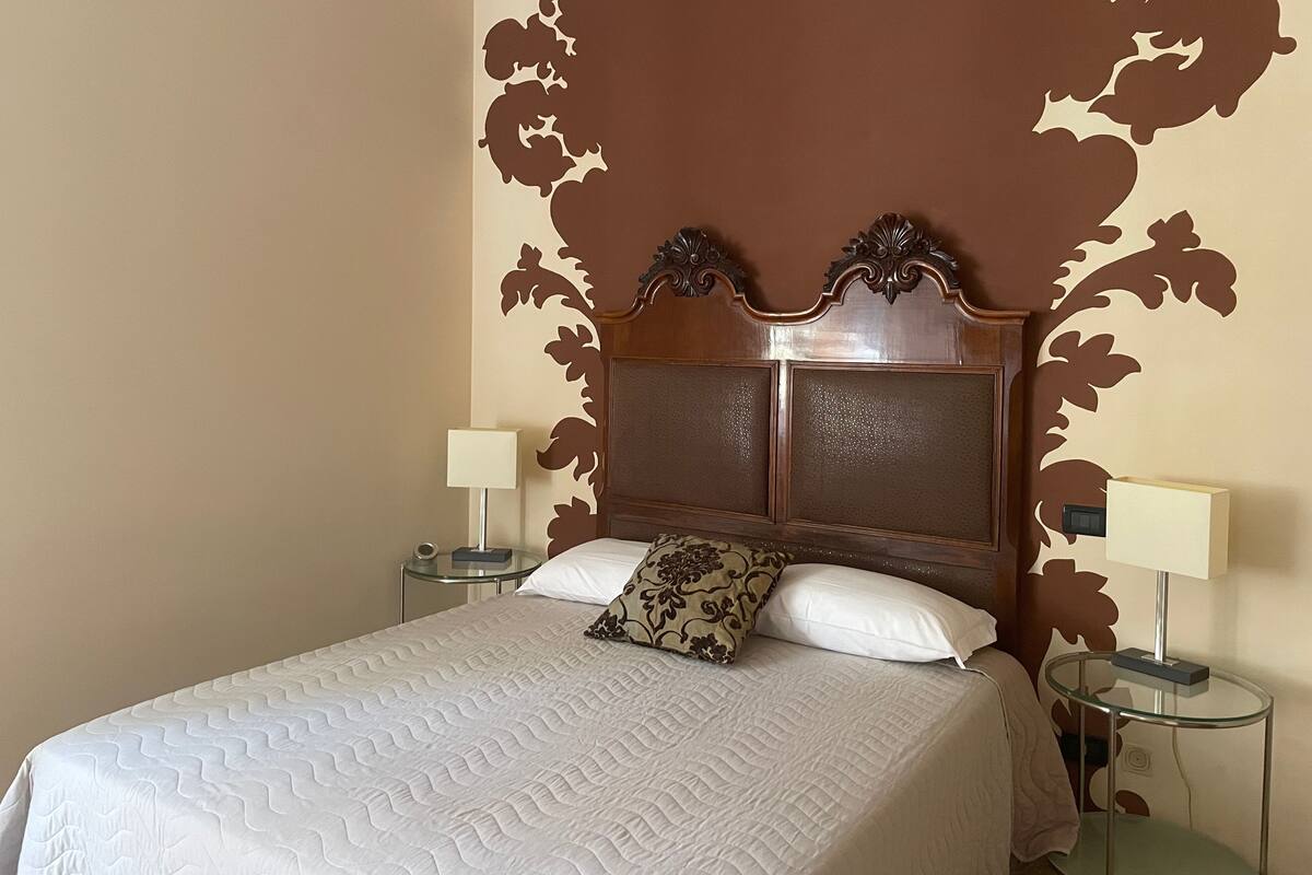 A neatly made bed with a white quilt, two bedside tables with lamps, and a wooden headboard with decorative carvings.