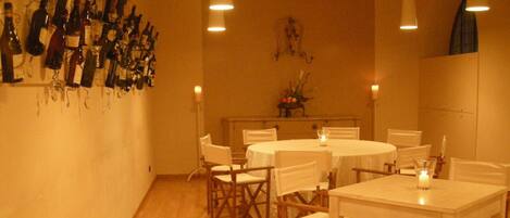 A dining area with white tables and chairs, a wall of wine bottles, and candles on the tables.