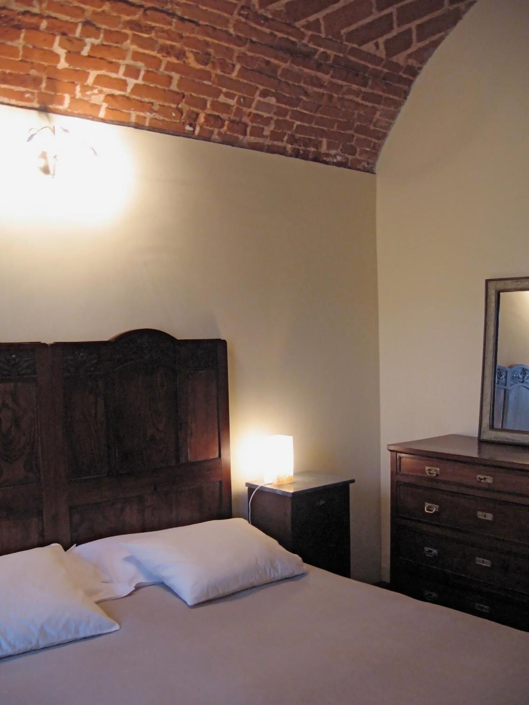 A bedroom with a wooden headboard, a bedside lamp, a dresser, and a mirror.