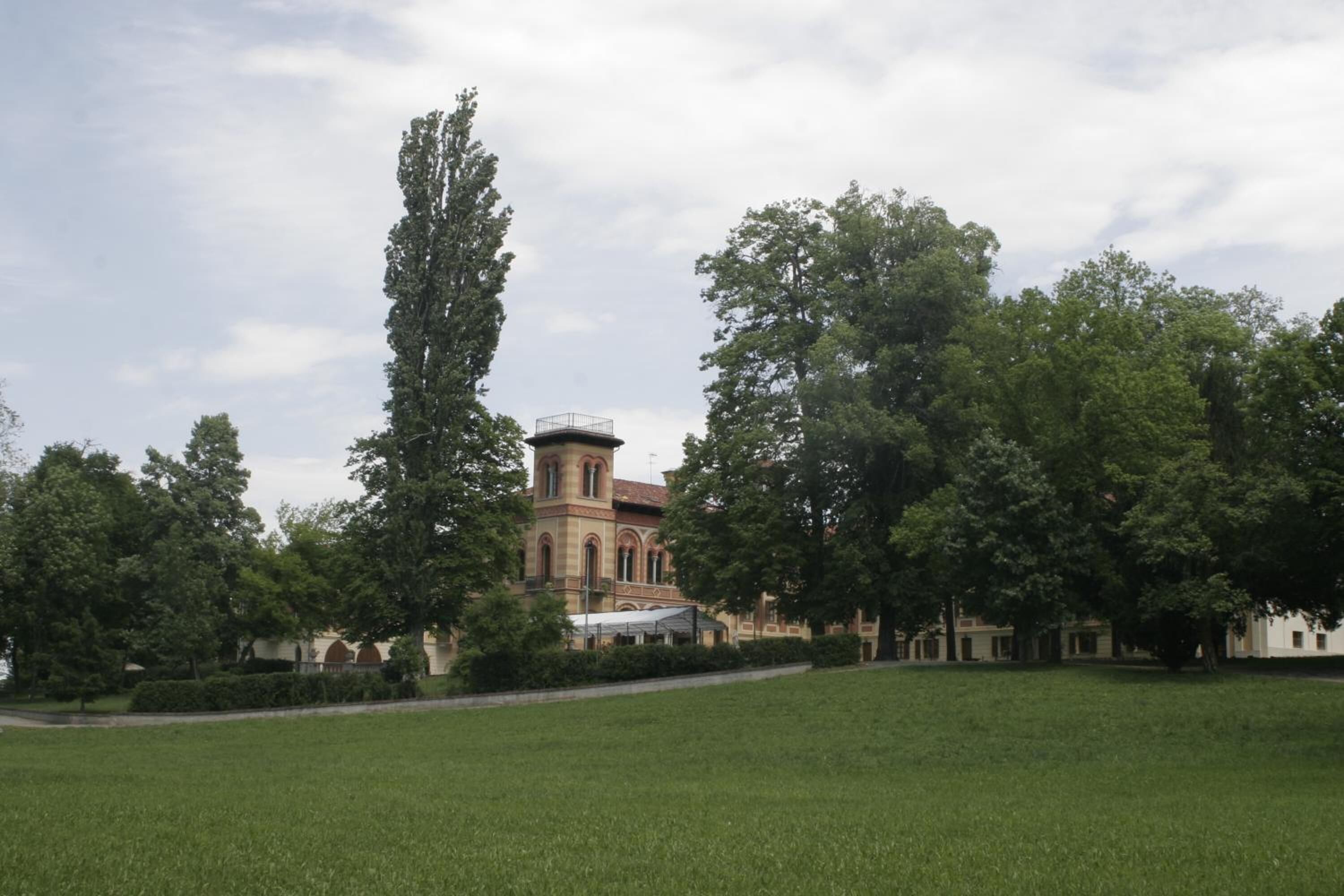 Ein großes, historisches Gebäude mit einem Turm, umgeben von einer gepflegten Rasenfläche und hohen Bäumen.