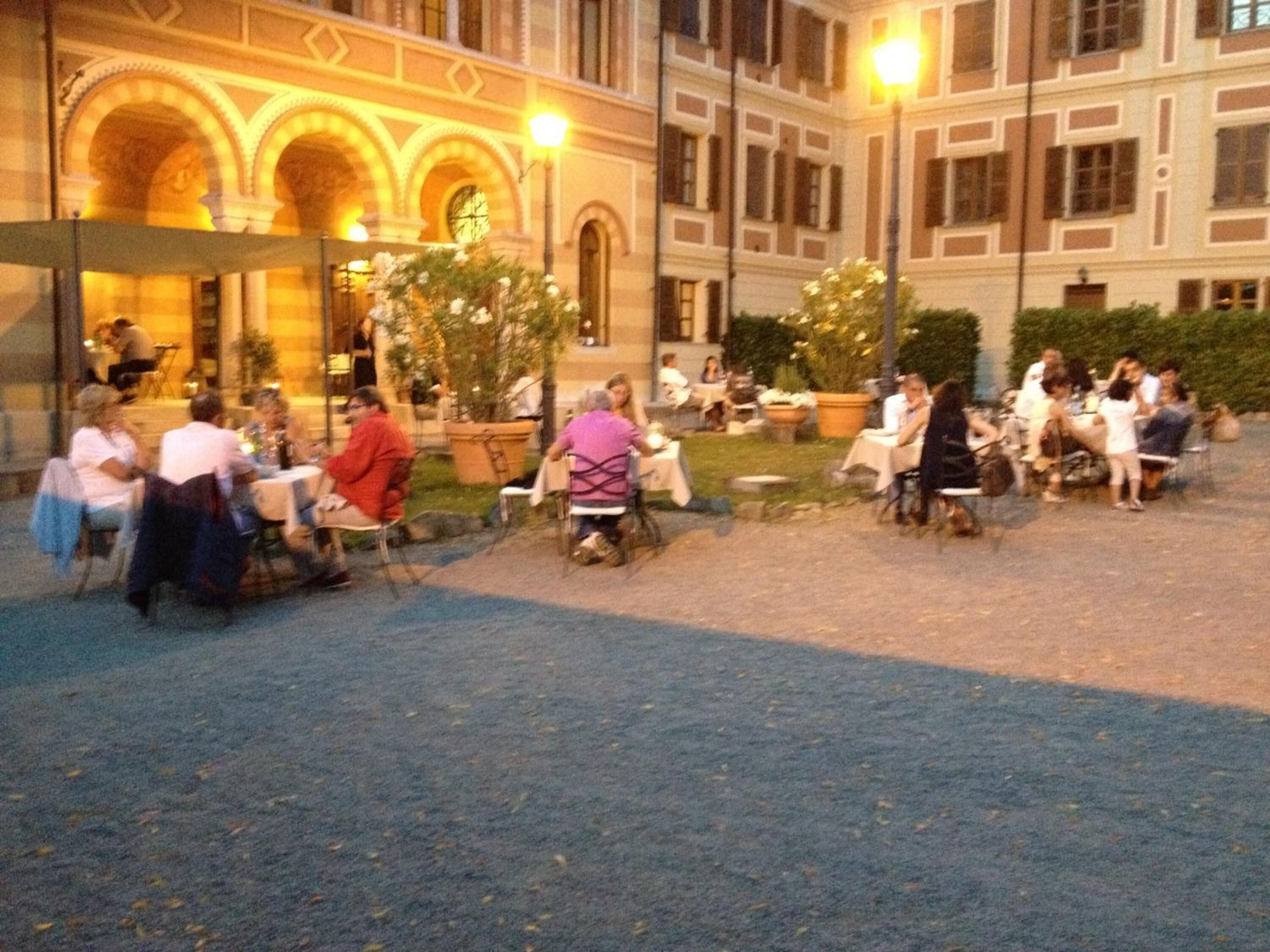 An outdoor dining area with tables and chairs, surrounded by a building with arched windows and a clock.