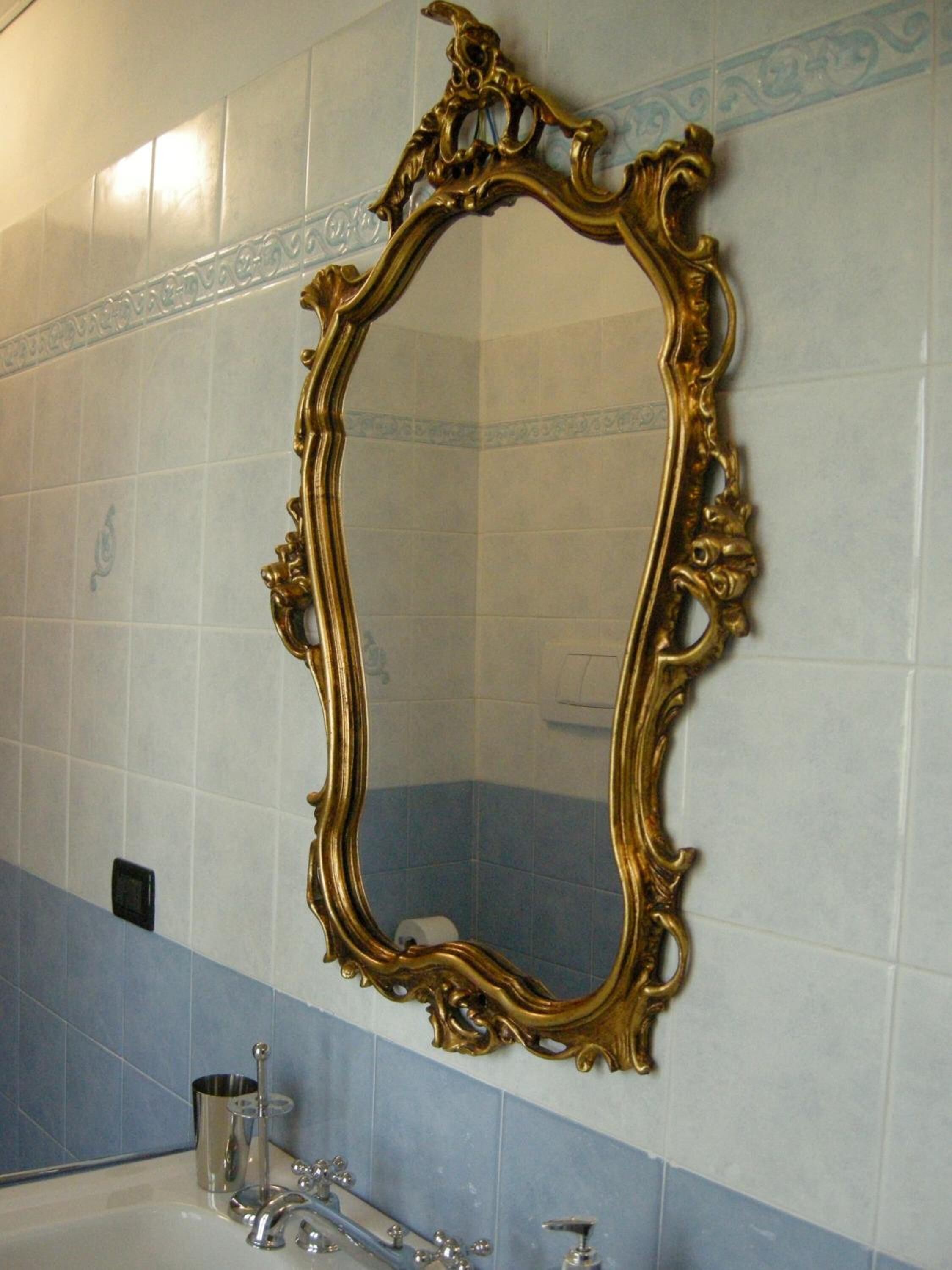 A bathroom with a large ornate gold-framed mirror, a sink with a modern faucet, and blue and white tiled walls.
