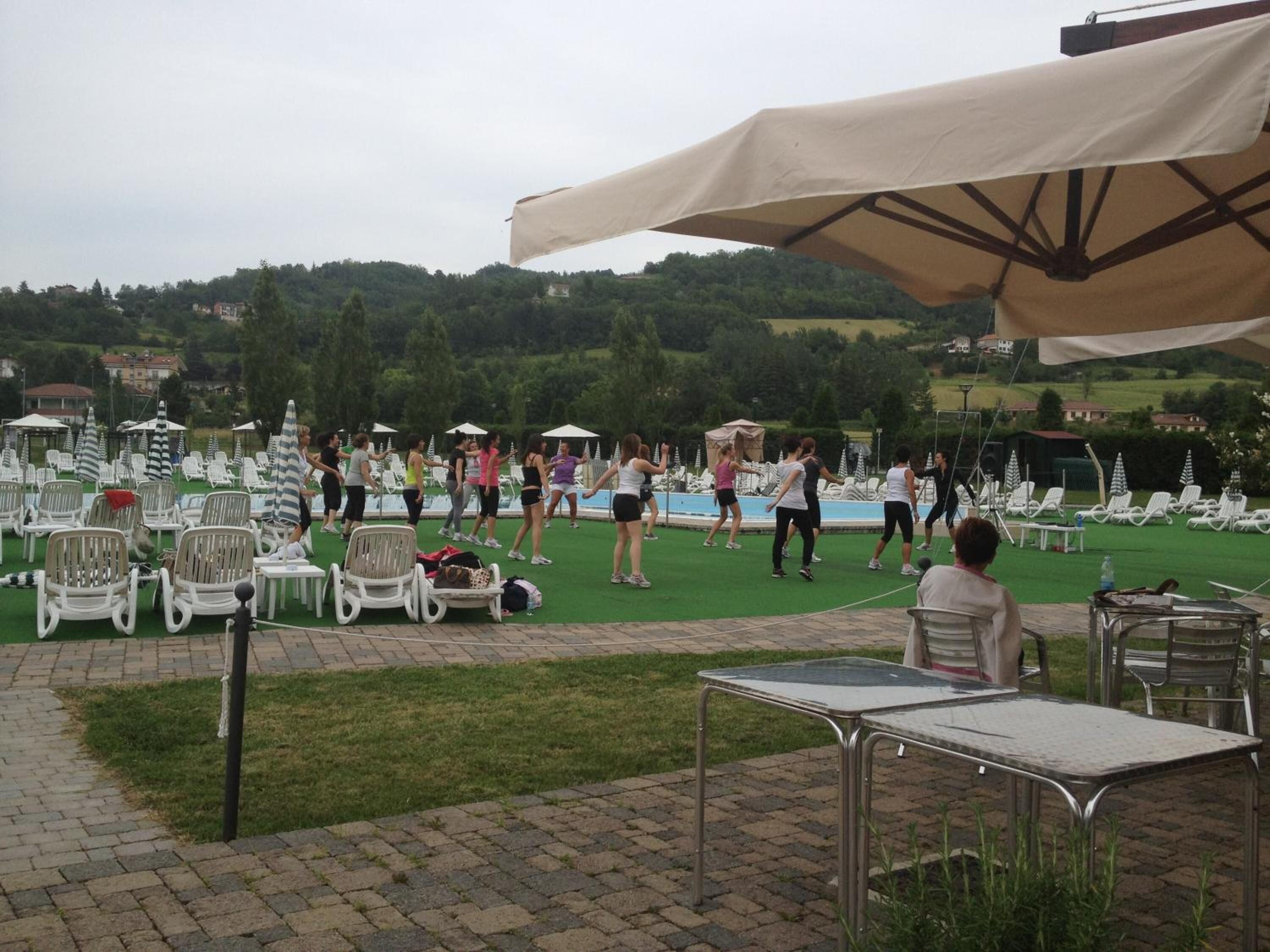 An outdoor area with lawn chairs and tables, a swimming pool, and a group of people exercising.