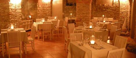 Un restaurante con paredes de piedra y techos abovedados, con mesas dispuestas con velas y copas de vino.