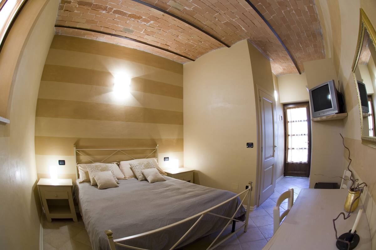A bedroom with a bed, bedside tables, a TV, and a bathroom door.